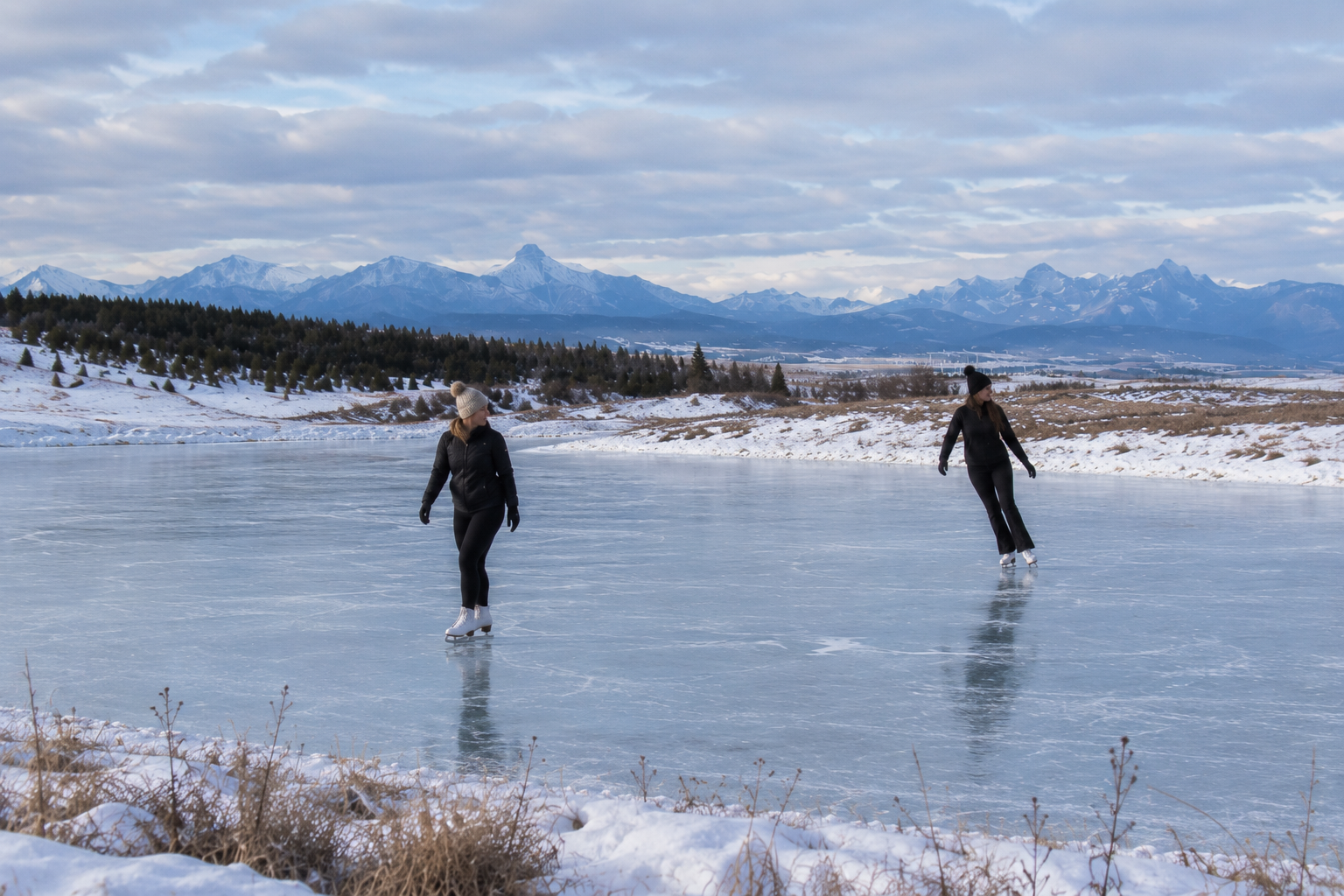 Two adults skating on a frozen winter lake beneath the mountains